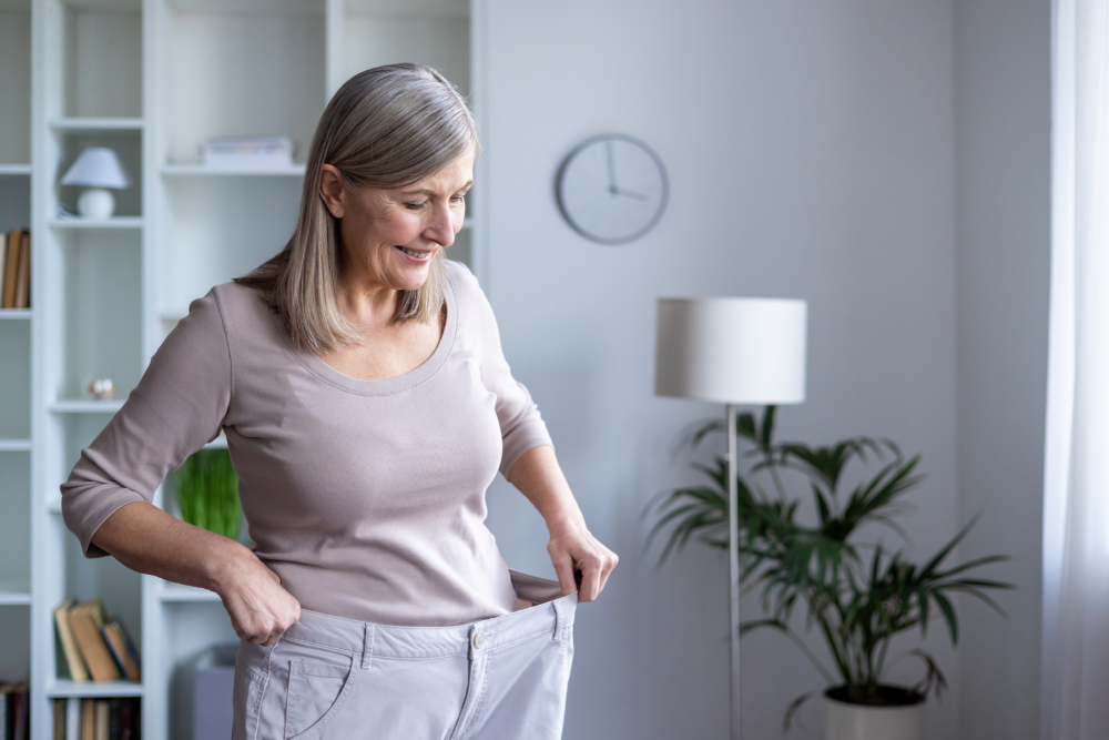 Senior woman showing loose pants after medical weight loss.